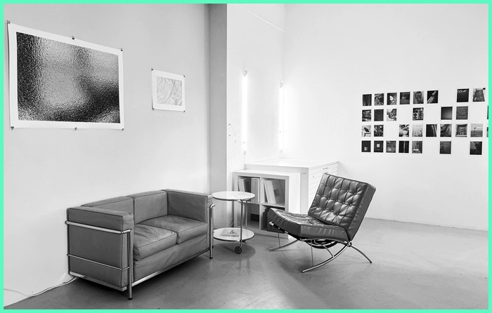 Sitzbereich im Atelier: Sofa und Sessel vor einer Wand mit gerahmten Arbeiten und einer Reihe kleiner Fotografien.